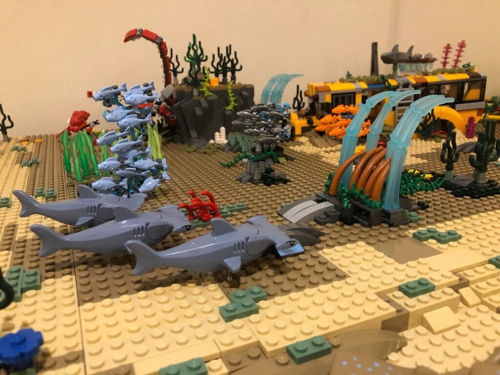  Representación Lego de un fondo marino con peces, tiburones, corales y un autobús escolar hundido. 